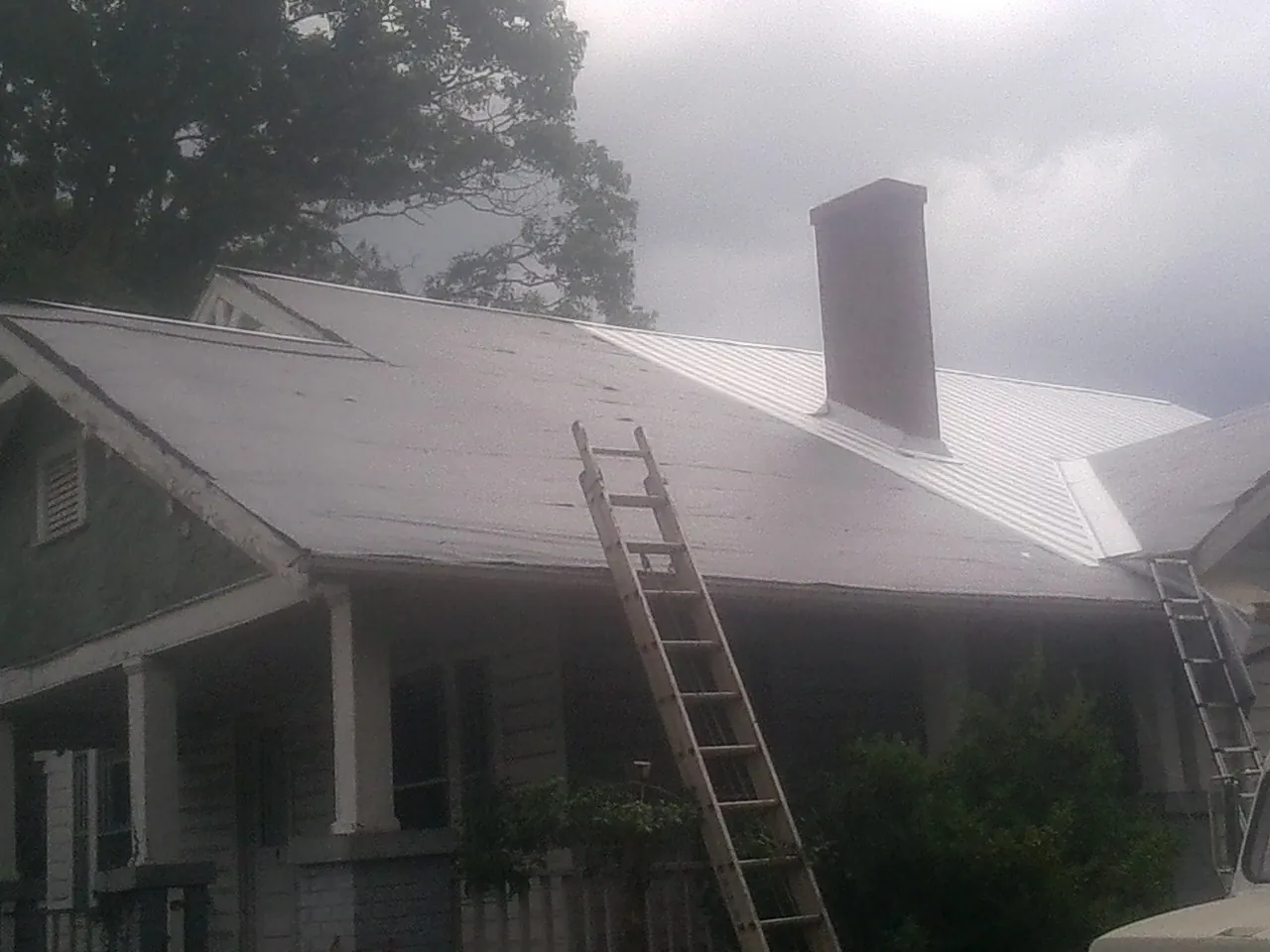 Ladders against a metal roof on an older home with a brick chimney in Arlington